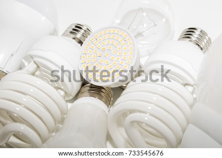 Several different led bulbs and compact fluorescent lamps with the size of the male screw base E27 on a light background