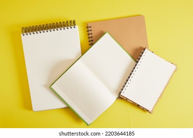 Several Different Notebooks For Sketching And Writing With Brown Craft Sheets On A Yellow Background, A Notebook With Aspiral And Binding, Mockup Top View