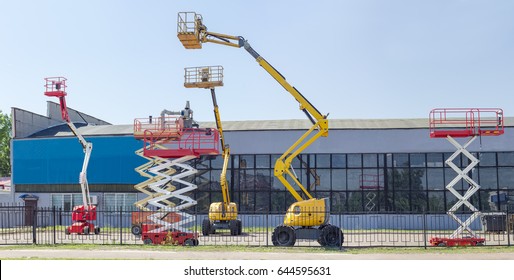 Several different wheeled scissor lifts and wheeled articulated lifts with telescoping boom and basket on an asphalt ground against the sky and an industrial building - Shutterstock ID 644595631