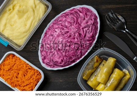 Several dishes in plastic boxes for breakfast on a wooden table, close up, top view. Mashed potatoes, beet salad with mayonnaise, grated carrots and wrapped pancakes in plastic food containers