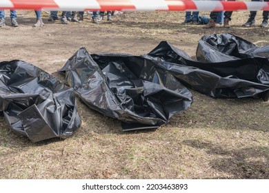 Several empty corpse body bag lie on the ground. People gathered around. - Shutterstock ID 2203463893