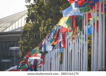 Several flags from different countries are seen flying on poles. The scene is set outside a contemporary building. It is a sunny day with clear skies