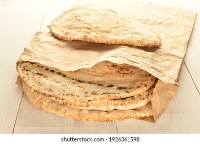 Several Freshly Baked Pita Bread In A Paper Bag, Close-up, On A Wooden Table.