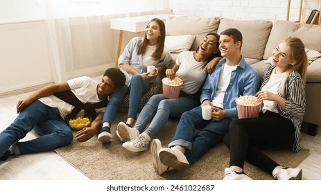 Several friends sitting on the floor together, each holding a bag of popcorn and eating. The group appears relaxed and engaged in conversation as they enjoy their snacks. - Powered by Shutterstock