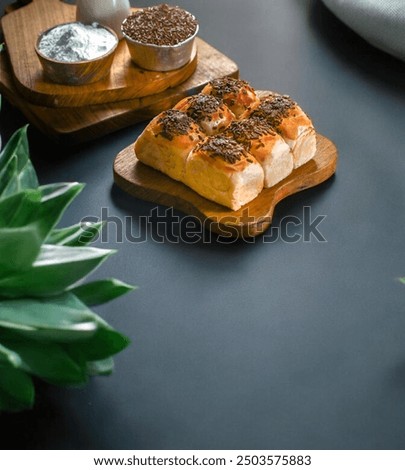 Several golden-brown bread rolls, drizzled with chocolate and cheese,arranged on a wooden board,a brown toppings. Lush green leaves add a touch of freshness,delightful spread on a black background