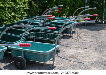 Several green plastic handcarts in front of a beech hedge