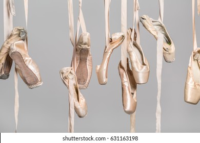 Several hanging beige ballet shoes on the gray background in the studio. Closeup. Horizontal.