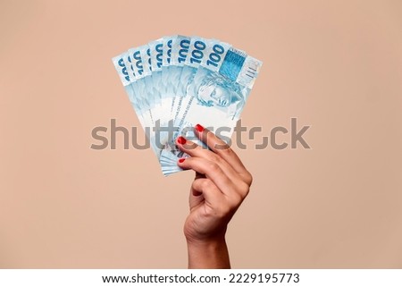 several hundred real bills - money from Brazil in a womans hand with red nails