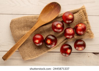 Several juicy black cherry tomatoes with wooden spoon and jute bag on wooden table, macro, top view.
