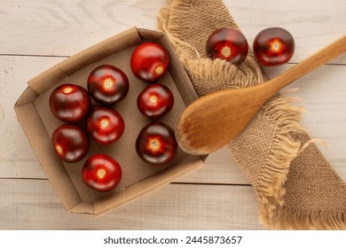 Several juicy black cherry tomatoes in paper plate, wooden spoon and jute napkin on wooden table, macro, top view.