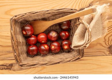 Several juicy black cherry tomatoes in a basket with a wooden spoon on a wooden table, macro, top view.