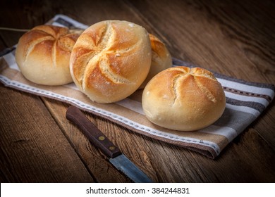 Several kaiser rolls on a wooden table.