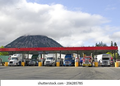 Several large over the road semi-trucks fuel up at a fueling station truck stop in California
