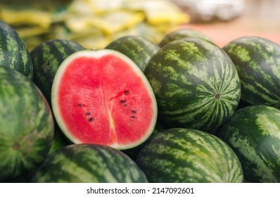 Several large sweet green watermelons and cut watermelons, several large sweet green watermelons are placed on a wooden table on a natural background for sale.