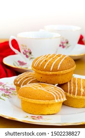 Several Lemon Drizzle Cakes With Icing On A Floral Pattern Bone China Plate With Several Cups The Background And A Red Cloth