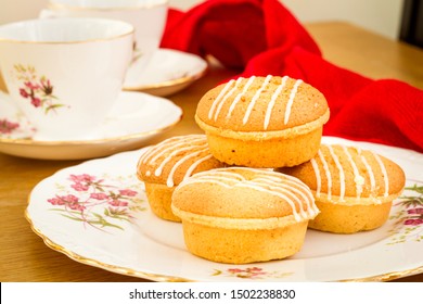 Several Lemon Drizzle Cakes With Icing On A Floral Pattern Bone China Plate With Several Cups The Background And A Red Cloth