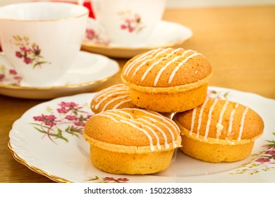 Several Lemon Drizzle Cakes With Icing On A Floral Pattern Bone China Plate With Several Cups The Background And A Red Cloth