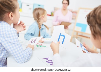 Several Little Kids With Paper Cards With English Letters Listening To Their Teacher At Lesson In Kindergarten