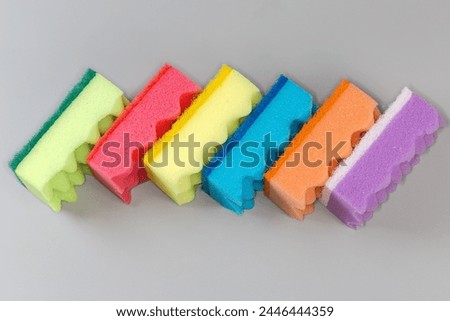 Several multi colored kitchen soft synthetic cleaning sponges with hard urethane abrasive layer laid out on a gray surface
