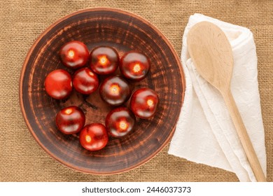 Several organic black cherry tomatoes with clay plate, wooden spoon and napkin on jute cloth, macro, top view.