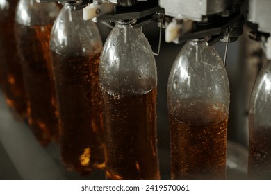 Several plastic bottles hanging on belt conveyor or assembly line during process of filling soda or lemonade before packaging - Powered by Shutterstock