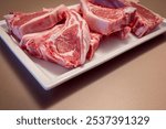 Several raw lamb chops placed on a white plate display fresh pink meat and fat layers The marbled texture emphasizes the quality of the lamb cuts prepared for cooking