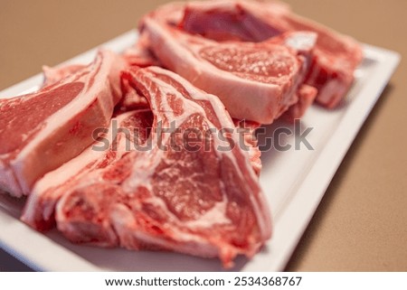 Several raw lamb chops placed on a white plate display marbled pink meat with visible fat The fresh cuts highlight their tenderness and readiness for cooking