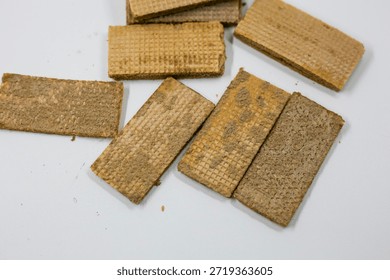 Several rectangular brown wafer cookies with crumbly texture are randomly scattered on a bright white table surface above.