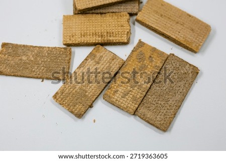 Several rectangular brown wafer cookies with crumbly texture are randomly scattered on a bright white table surface above.
