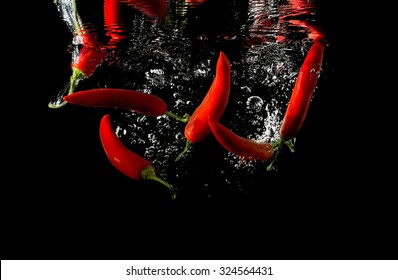 Several red peppers fallen into the water isolated on the black background