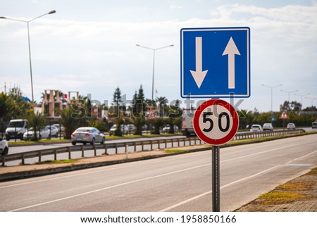 Several road signs: speed limit within 50 km per hour and regulation of traffic in lanes in the background of a motorway with trees