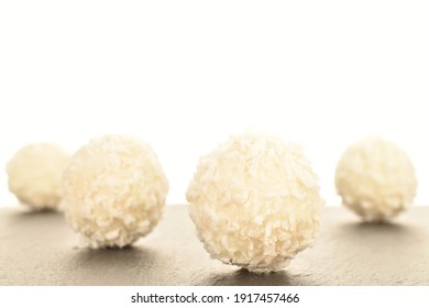 Several round sweets with coconut flakes on a slate board, close-up, isolated on white.