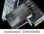 Several silver bars of different weight on a dark mirror surface. Selective focus.