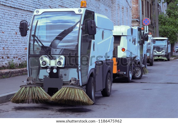 Several small cars for cleaning streets\
standing at the side of the road on a city\
street.