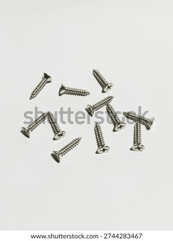 Several small silver Phillips-head screws are scattered randomly across a smooth white surface, each showing sharp pointed tips, deep spiral threads, and reflective metallic finishes under soft lighting.