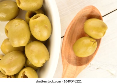 Several spicy tasty organic pickled green olives lie on a white ceramic saucer and a wooden spoon, close-up, on a background of natural, white painted wood, top view. - Powered by Shutterstock