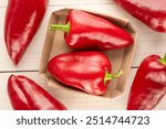 Several sweet red peppers with paper plate on wooden table, macro, top view.

