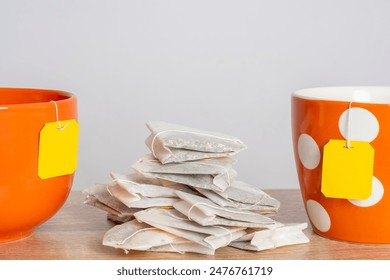 Several tea bags with empty yellow labels lie in a tea cup. Template with blank tag on the theme of hot soft drinks.