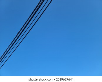 Several Thick Powerlines Running Across The Clear Blue Sky On A Sunny Day. The Electrical Wires Are Black, Long, And Thick.