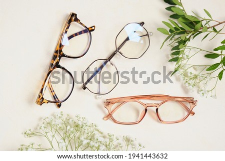 several trendy stylish glasses and flowers on a beige background place copy top view, optics, shop of glasses and frames concept