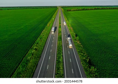 several trucks drive along the asphalt road along the green fields at sunset. seen from the air. Landscape from a bird's eye view. drone photo. delivery of cargo