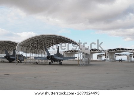 Several twin-engine multirole fighters aligned under canopy shelters at military airbase with open sky