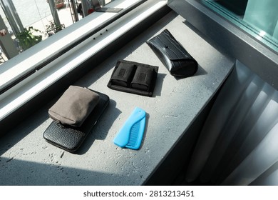 Several wallets and a comb are placed on a stone surface near a window. Bright sunlight filters through the glass, creating reflections.