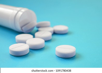 Several white tablets fall out of the plastic jar on the blue surface. Background image on medical and pharmaceutical topics