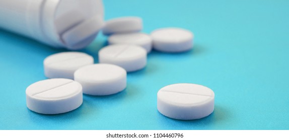 Several white tablets fall out of the plastic jar on the blue surface. Background image on medical and pharmaceutical topics