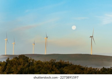 Several wind turbines or windmills at dawn, with the full moon in the background. - Powered by Shutterstock