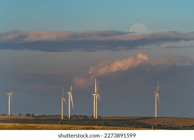 Several wind turbines or windmills at dawn, with the full moon in the background. - Powered by Shutterstock