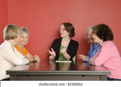 Several Women Sit Around A Table In Animated Conversation With A Group Leader Who Might Be An Instructor Or Facilitator
