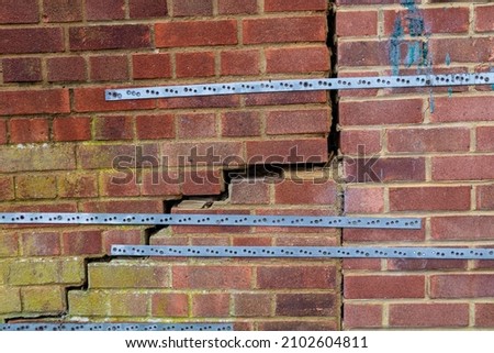 Severe cracking due to subsidence in a red brick wall held together by steel brackets