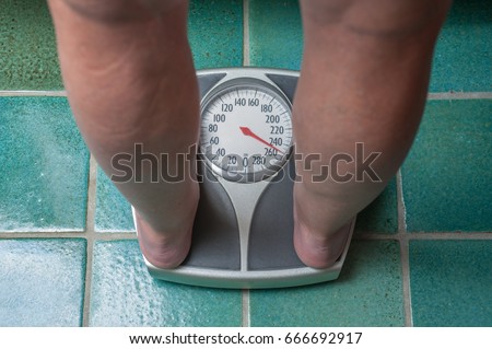 A severely overweight person weighing herself or himself on a bathroom scale